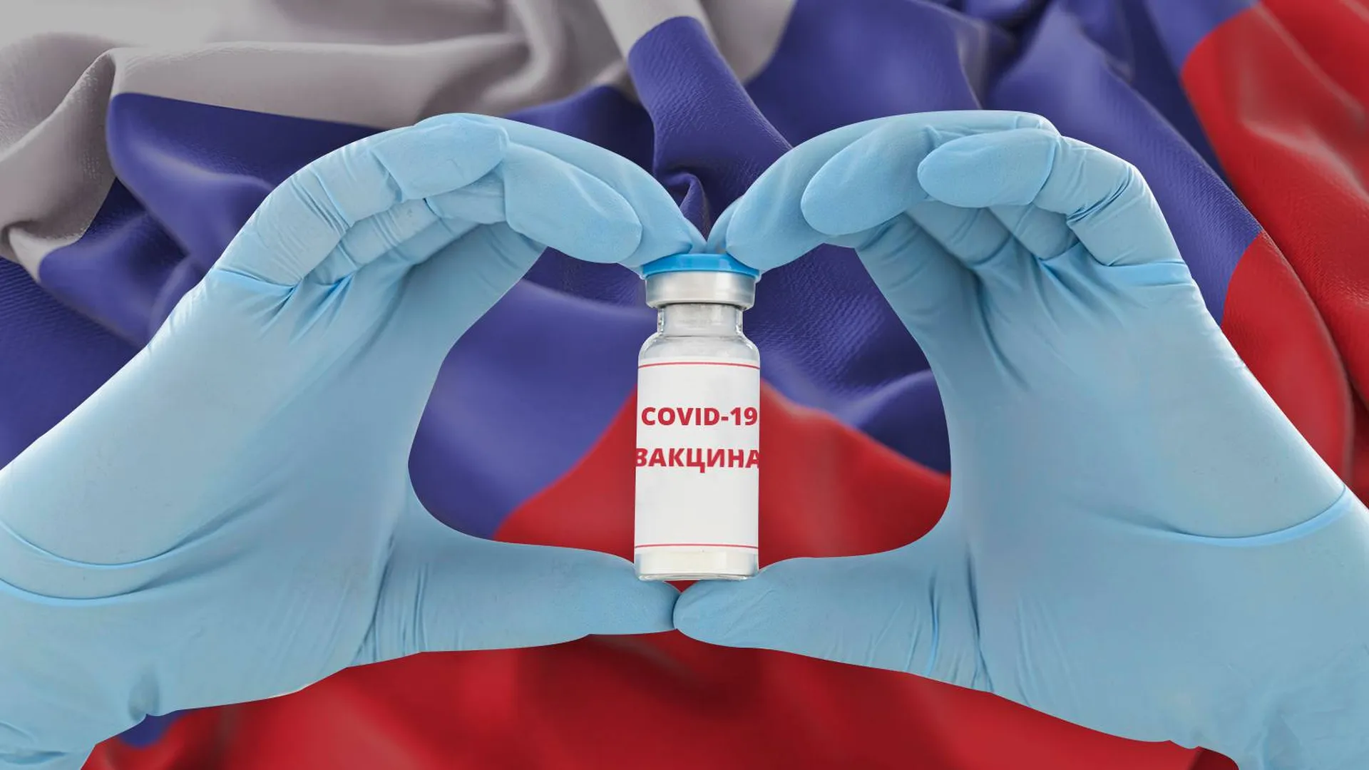 Руки в медицинских перчатках держат пузырек с вакциной от Covid-19 на фоне российского флага