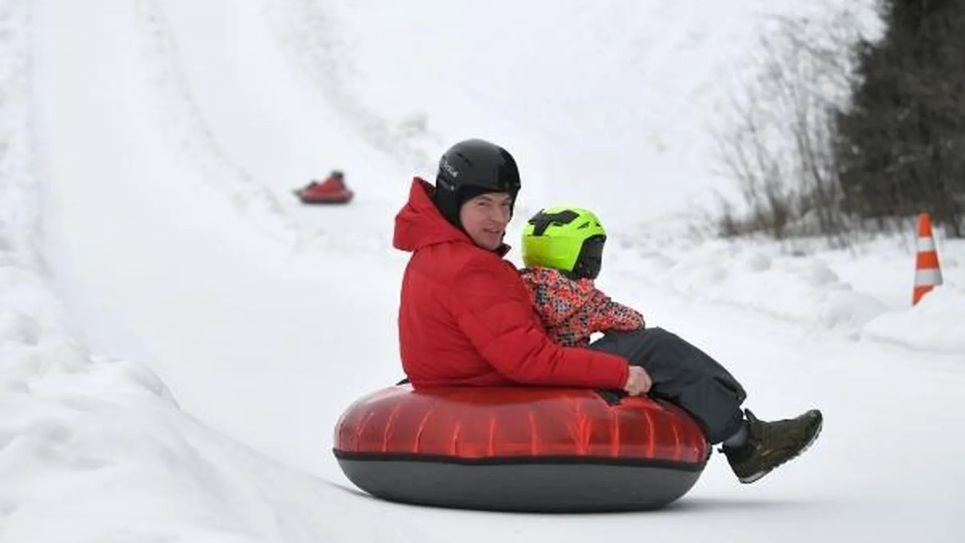 Мужчина с ребенком катаются на тюбинге на горнолыжном курорте «Сорочаны» в Московской области