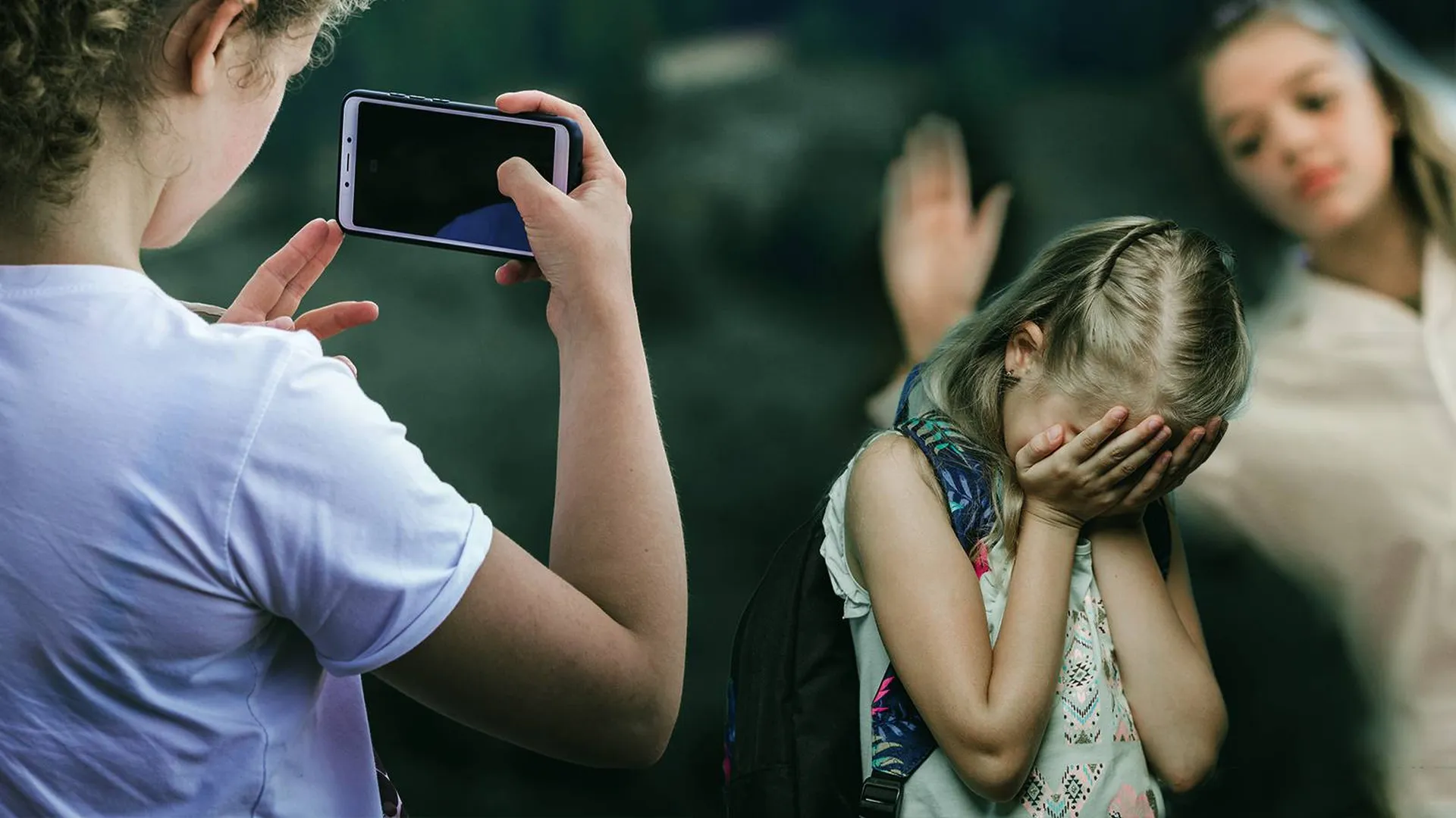 Плачущая девочка, которую другие дети снимают на смартфон