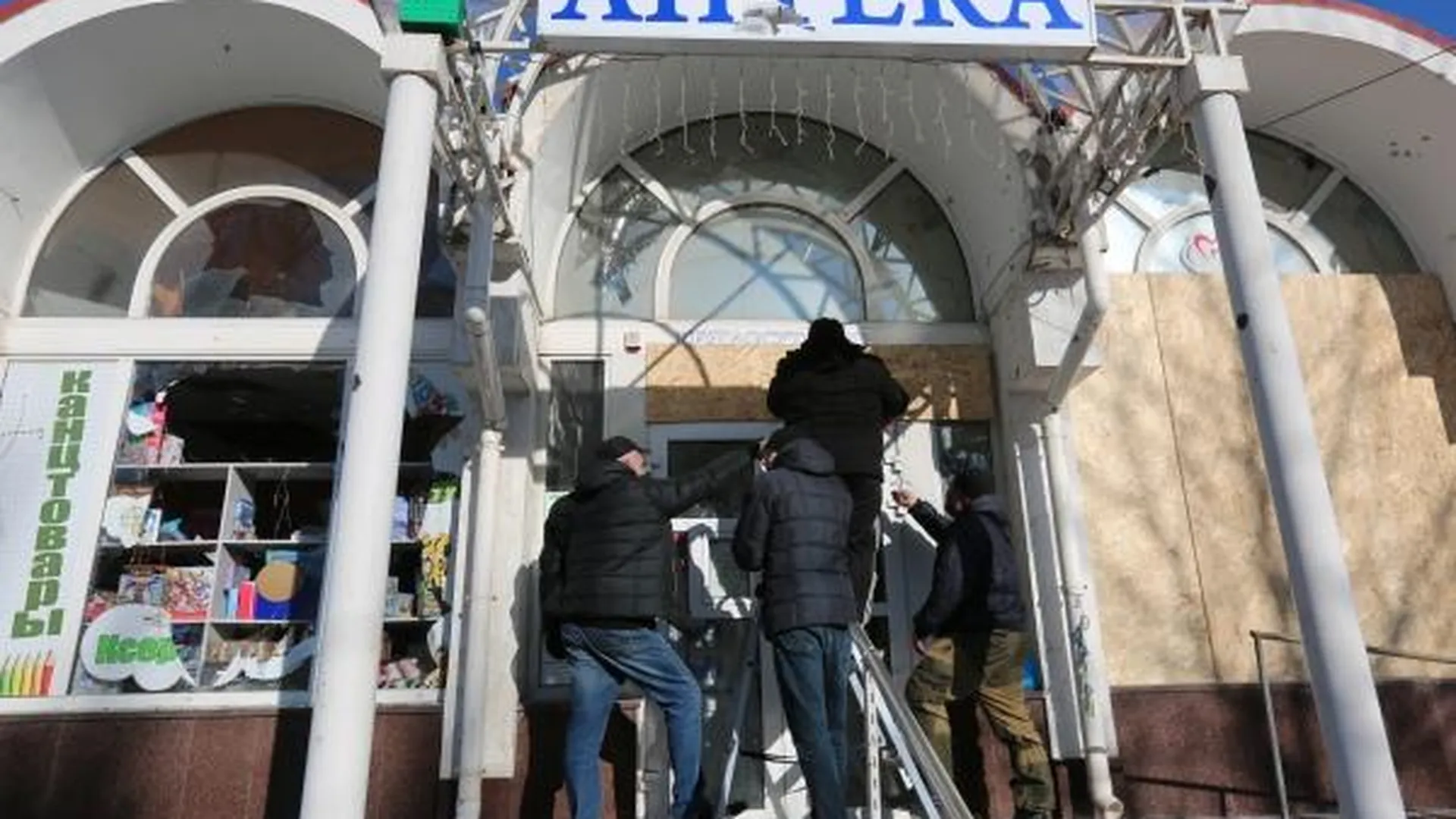 Мужчины ремонтируют здание аптеки, поврежденное в результате обстрела ВСУ рынка в Кировском районе Донецка.