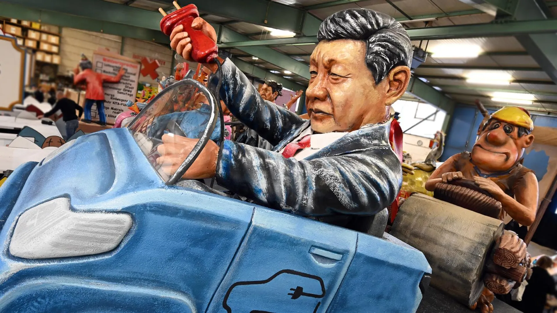 Фигуры для парада в Майнце: лидер партии Китая Си Цзиньпин в электромобиле, за которым еле тащится немец на машине Фреда Флинстоуна из каменного века. Фото: Arne Dedert