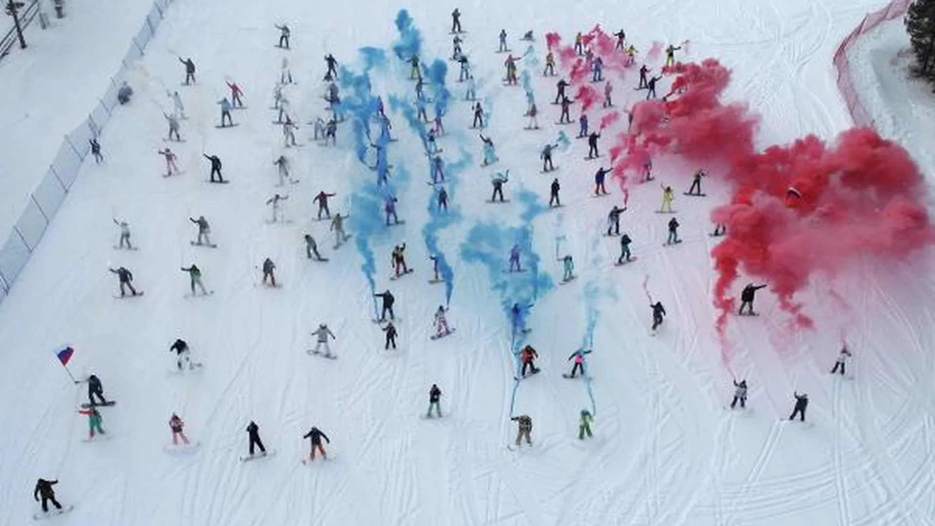 Массовый спуск на сноубордах c фальшфейерами в цветах российского государственного флага в поддержку российских спортсменов