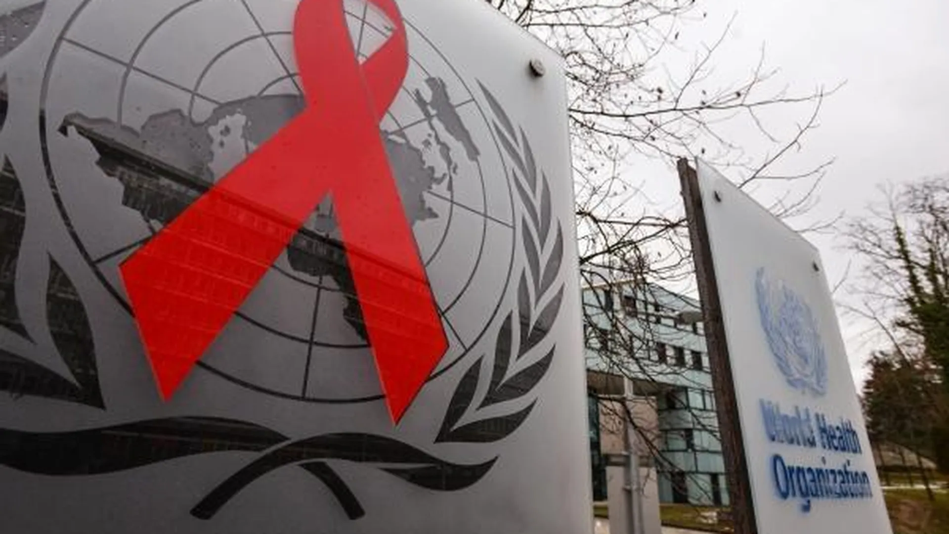 Эмблемы Всемирной организации здравоохранения и Объединенной программы ООН по ВИЧ/СПИД (ЮНЭЙДС) на входе в здание штаб-квартиры организации в Женеве